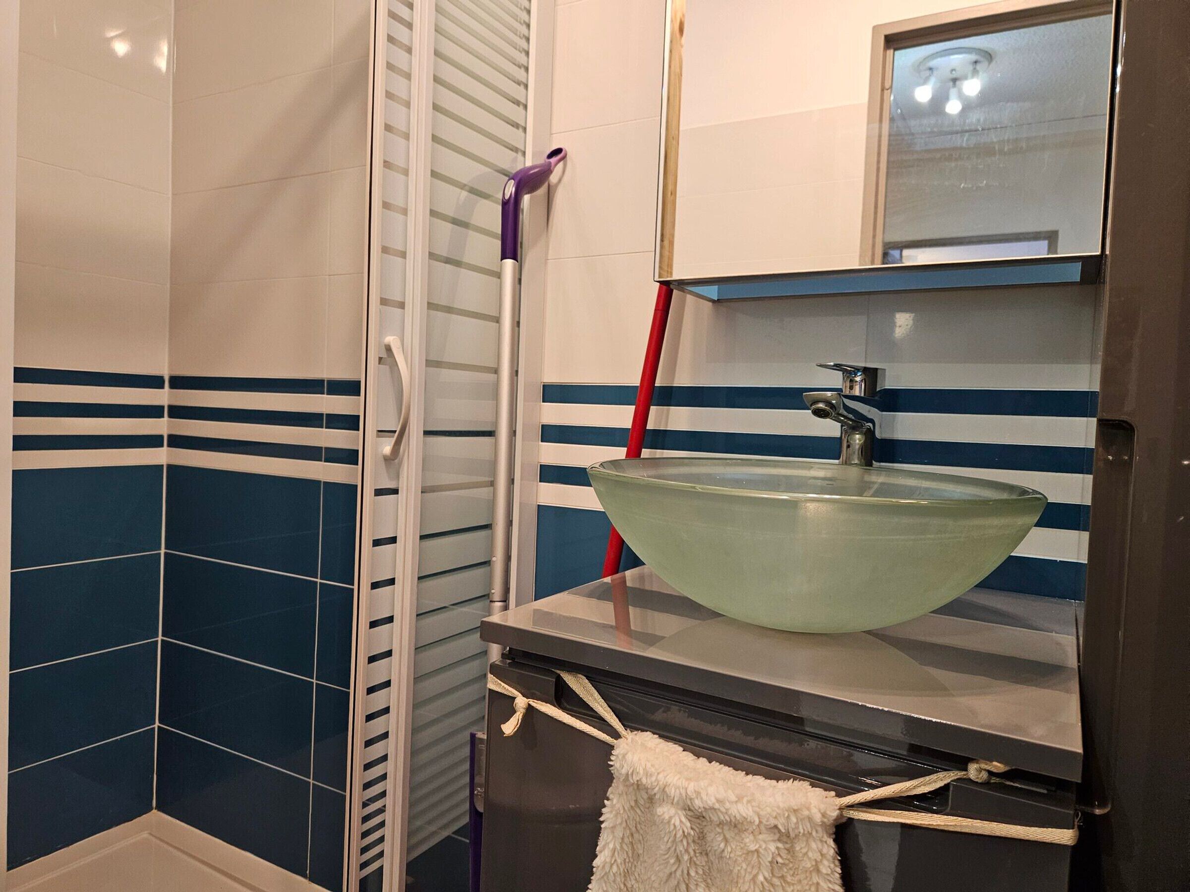 A bathroom with a glass sink, striped tiles, a towel, and a mirror.