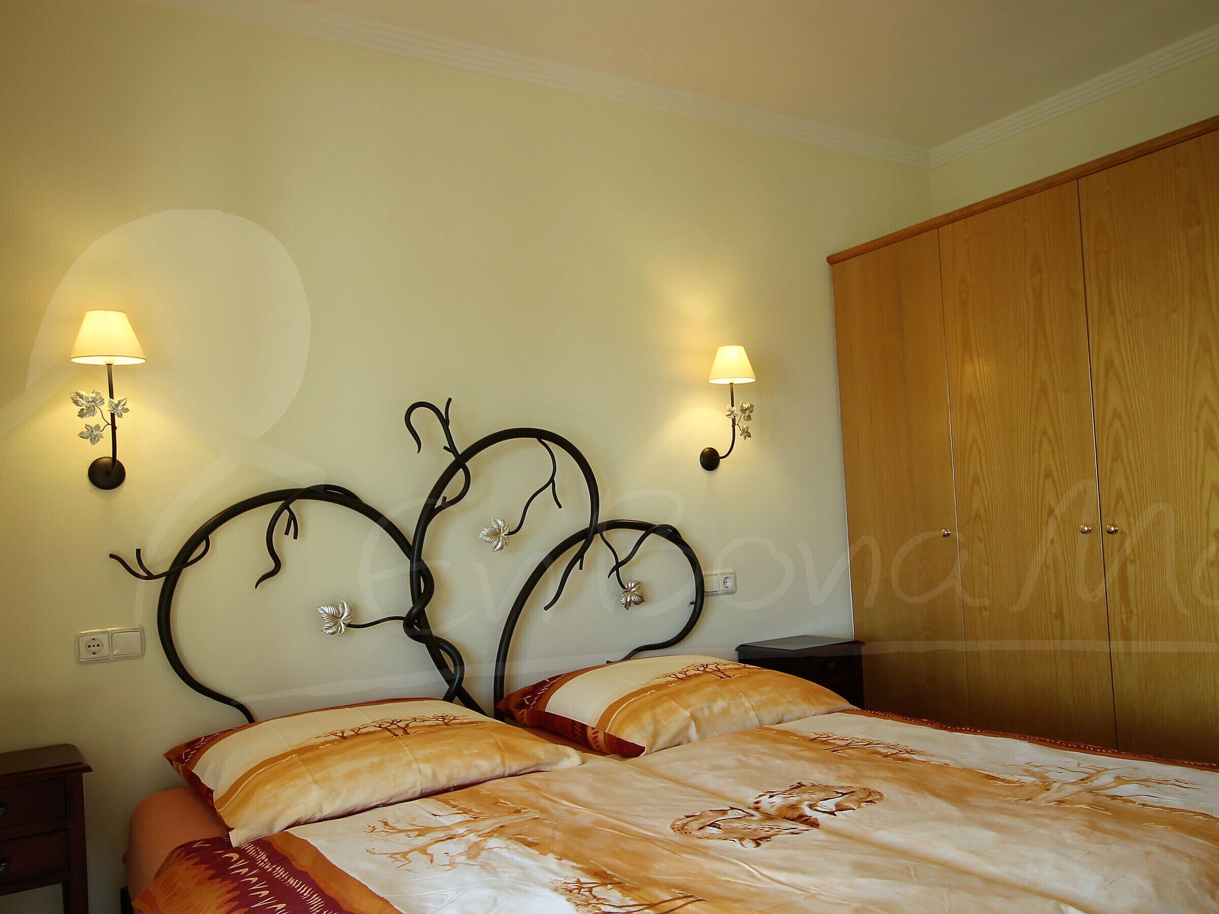 Un dormitorio con una cama, dos lámparas fijadas a la pared y un armario de madera.