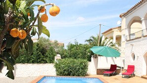 A swimming pool with a tiled edge, surrounded by a stone wall and a building with a balcony.