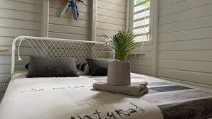 A neatly made bed with a "So Natural" pillow, a decorative wall piece, and a potted plant on the windowsill. - Villa ATOLA with swimming pool 800m from Le Diamant beach in Martinique. (Le Diamant)