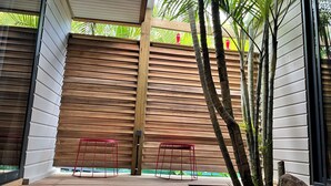 A modern outdoor patio with wooden slatted walls, two red chairs, and a small water feature. - Villa ATOLA with swimming pool 800m from Le Diamant beach in Martinique. (Le Diamant)