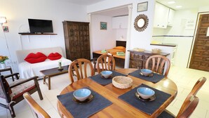 Zona pranzo con un tavolo in legno apparecchiato per quattro persone, circondato da sedie. Si intravede, sullo sfondo, un divano con cuscini rossi.