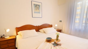 Un letto rifatto con lenzuola bianche, una testiera in legno e un comodino con una lampada.