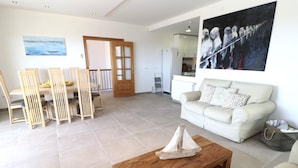 Una sala de estar con una mesa de centro de madera, un sofá blanco y una zona de comedor con sillas y una mesa de madera.