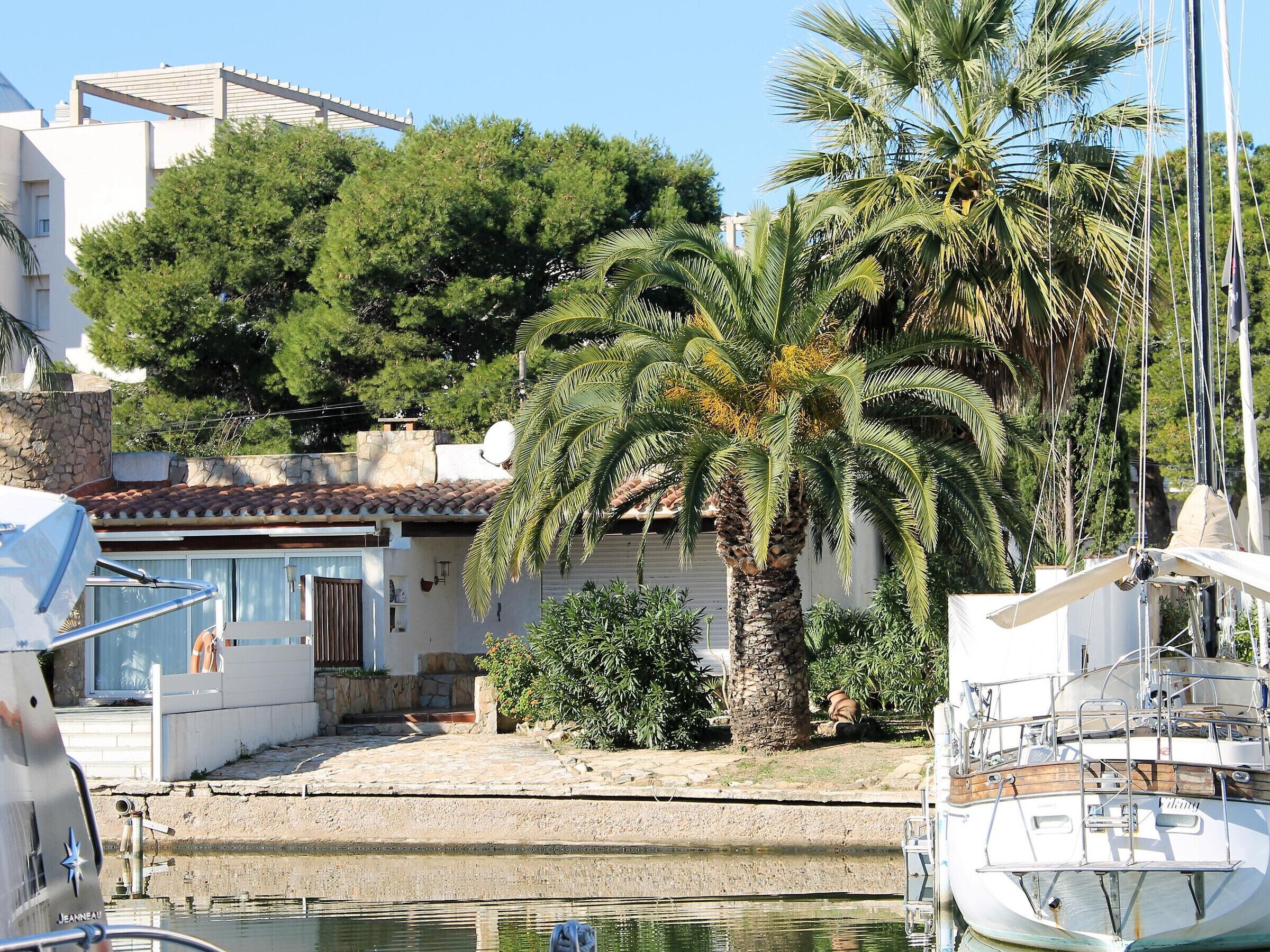 A marina with boats docked, a palm tree, and a building with a tiled roof.