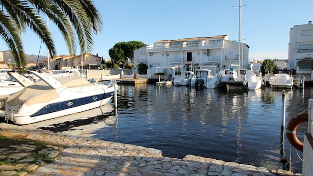 A marina with boats docked, a white building with balconies, and a stone-paved walkway. - Charming House by the Canal with Terrace - Roses (Roses)