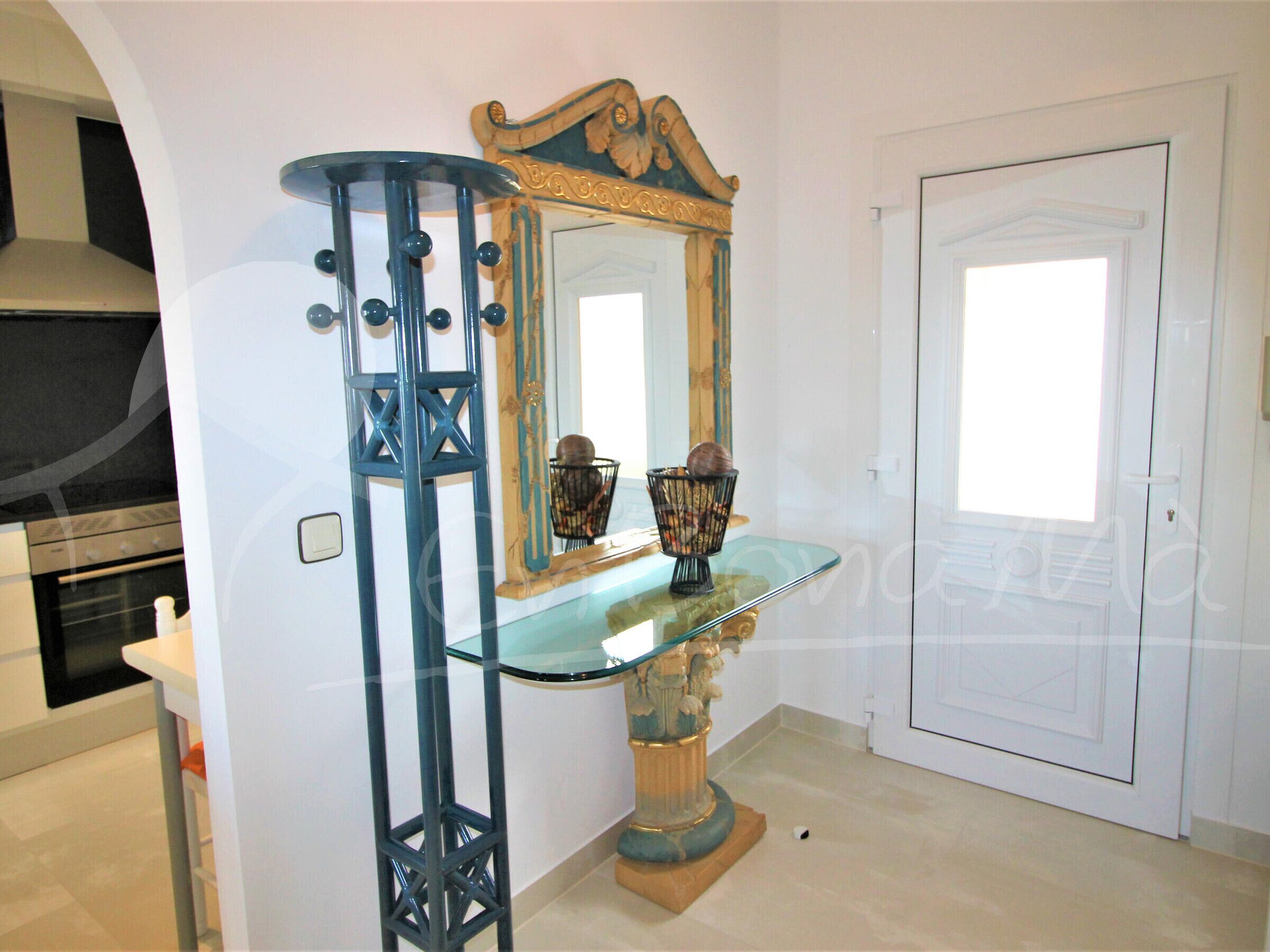 Una habitación con una mesa consola de vidrio, un espejo decorativo y una puerta.