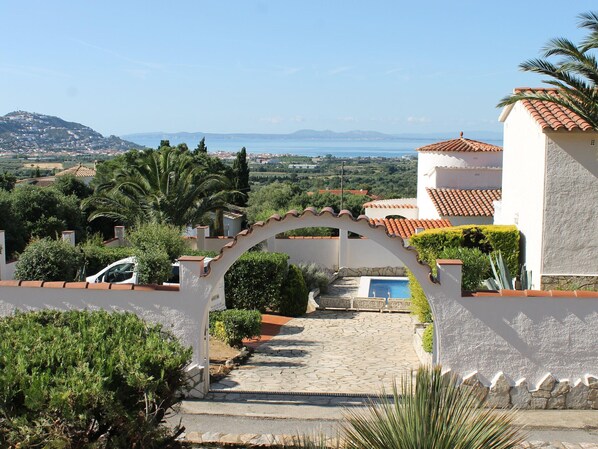 Una villa con un sendero de piedra que lleva a una piscina, rodeada de exuberante vegetación y una vista panorámica del mar.