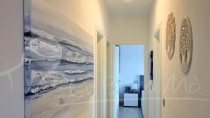 Un pasillo con un gran cuadro abstracto a la izquierda, una puerta que da a un dormitorio y decoración en las paredes a la derecha.
