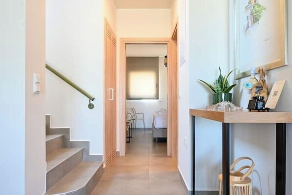A hallway with a staircase leading to a room with a bed and a desk.