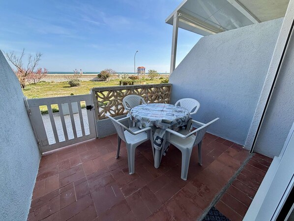 A patio with a table and chairs, a view of the sea, and a white fence.