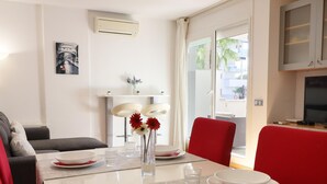 A dining area with a table set for four, a vase with flowers, and a view of the outside.