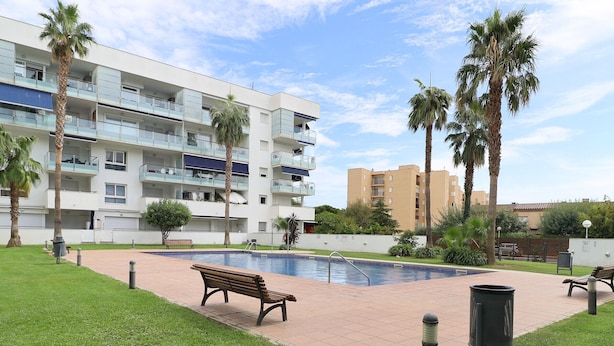 A residential building with balconies, a swimming pool, and palm trees.