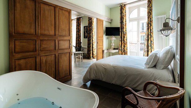 A bedroom with a large bed, a bathtub, and a wicker chair. - Charming air-conditioned apartment, central Pézenas, pets welcome (Pézenas)