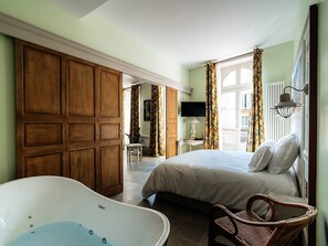 Une chambre à coucher avec un grand lit, une baignoire et un fauteuil en osier.