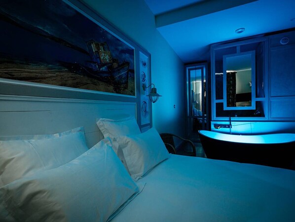 A hotel room with a bed, a nightstand, a desk, and a large window.