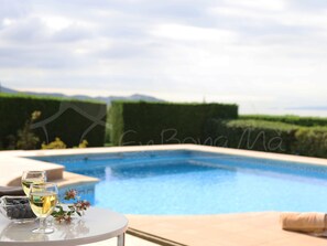 Escena junto a la piscina con una mesa que sostiene dos copas de vino blanco, un cuenco de arándanos y un pequeño arreglo floral.