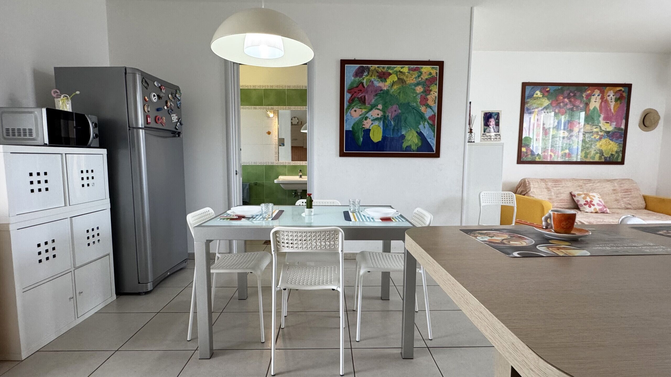 A modern kitchen with white cabinets, a stainless steel refrigerator, and a dining area with a table and chairs.