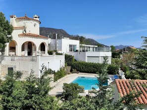 Una villa moderna con piscina, rodeada de exuberante vegetación y con vista a la montaña.