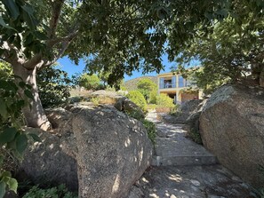Una escala de pedra que condueix a un edifici envoltat de roques grans i arbres.