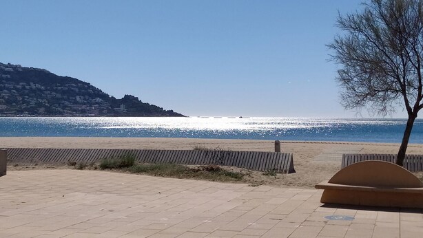 A paved walkway leading to a beach with a clear view of the sea and a hill with buildings in the background. - Modern 2-bedroom apartment with private garden 100m from beach (Roses)
