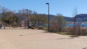 A paved walkway with exercise equipment, trees, and a clear view of a body of water and hills in the background. - Modern 2-bedroom apartment with private garden 100m from beach (Roses)