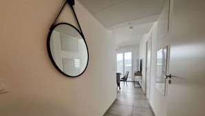 A hallway with a round mirror, a door, and a view of a balcony with a chair and a table. - Beautiful new apartment for 4 with terrace, Cap d'Agde (Cap d'Agde)