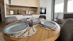 A modern dining area with a round table set for four, a coffee machine, and a view of the city through large windows. - Beautiful new apartment for 4 with terrace, Cap d'Agde (Cap d'Agde)