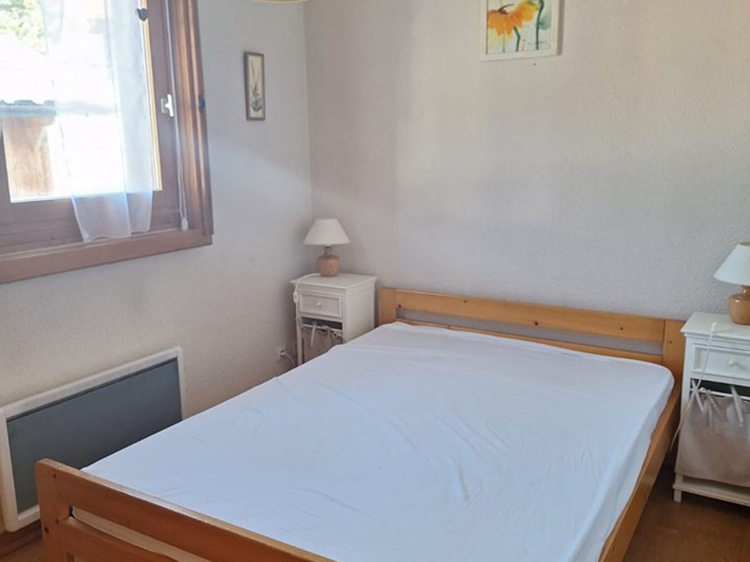 Et soveværelse med en træseng, et natbord med lampe, en radiator og et vindue med gardiner.