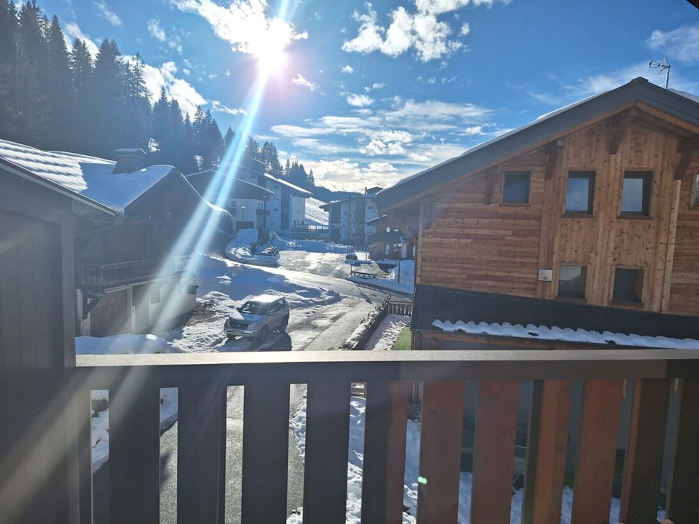 A wooden cabin with a snow-covered roof, a clear sky, and a sun shining through the clouds.