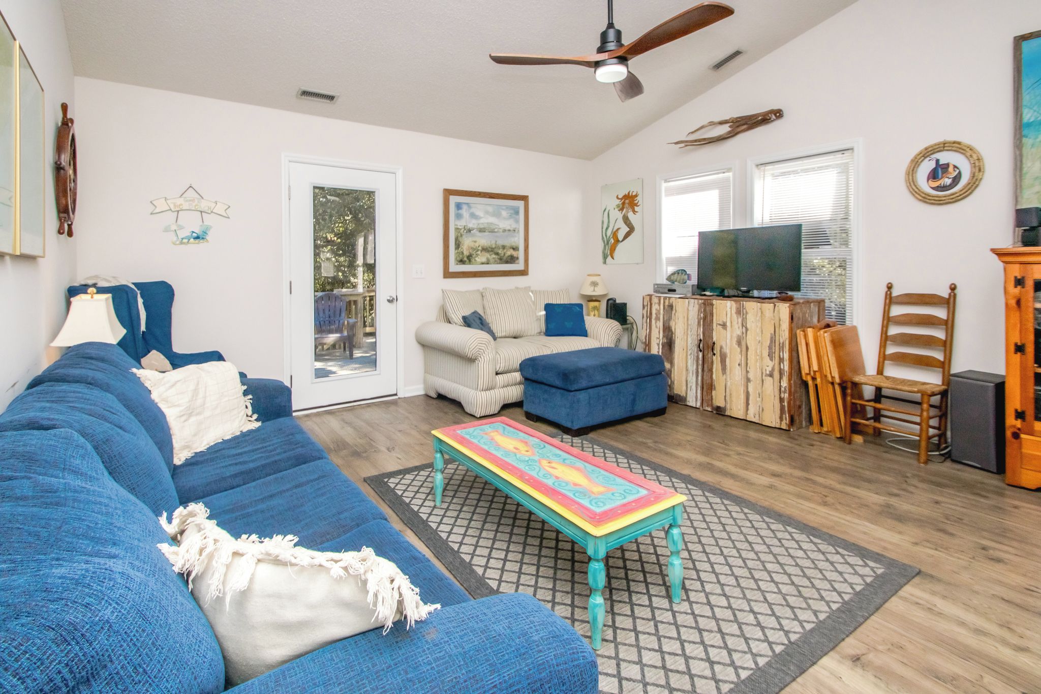 A living room with a blue sofa, a colorful coffee table, and a television on a wooden cabinet.