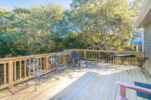 A wooden deck with metal chairs and a table, surrounded by trees.