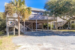 A two-story building with a covered outdoor area, a gravel driveway, and a palm tree.
