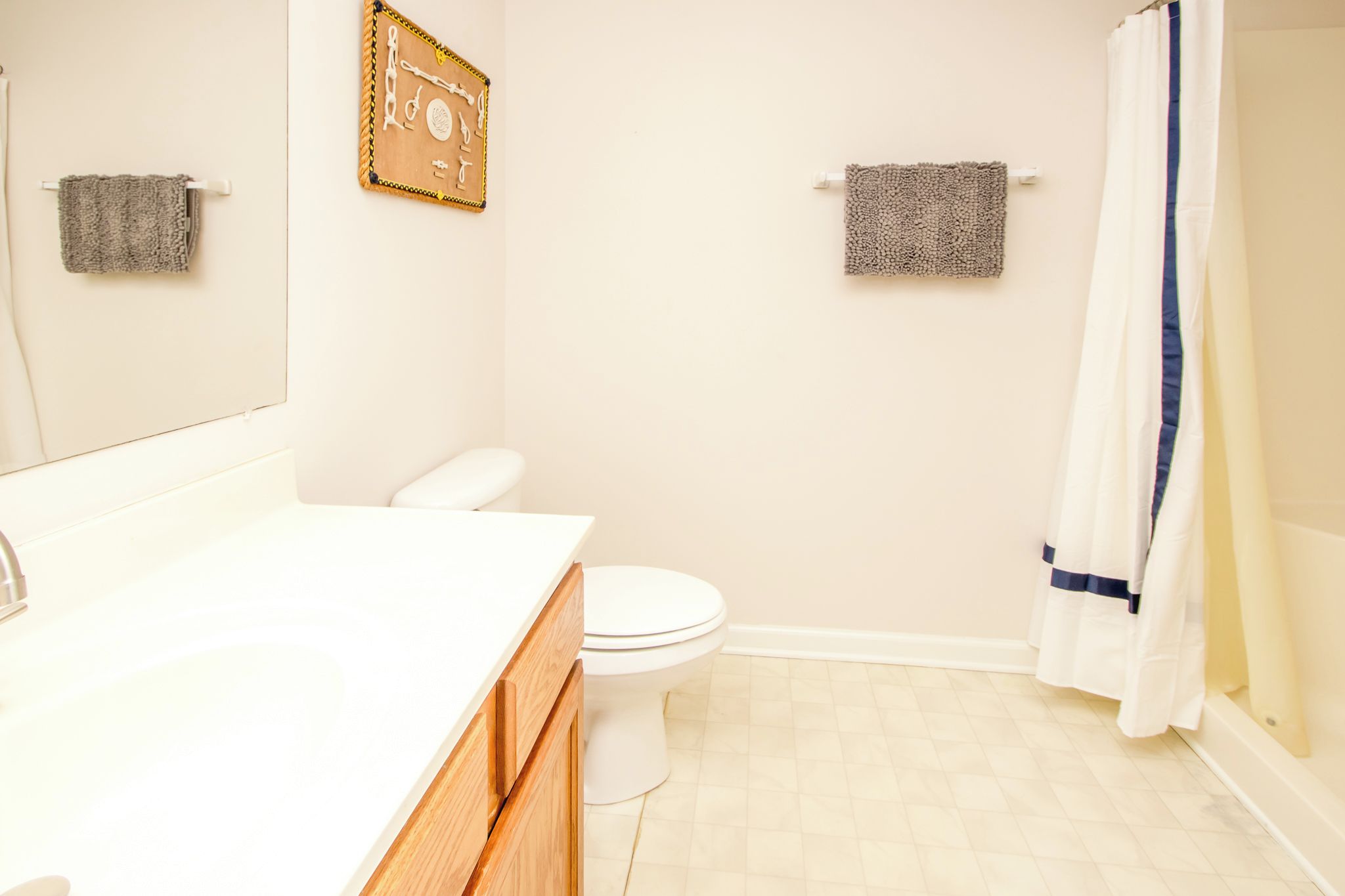 Une salle de bain avec des toilettes blanches, un meuble-lavabo en bois, un porte-serviettes avec deux serviettes et un rideau de douche.