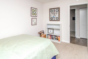 A bedroom with a bed, a bookshelf, and framed items on the wall. - It Must Be The Wine - 3BR Home in Quiet Spot. Pet Friendly! (Topsail Beach)
