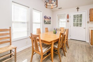 Uma sala de jantar com mesa e cadeiras de madeira, um lustre e uma porta com uma cruz.