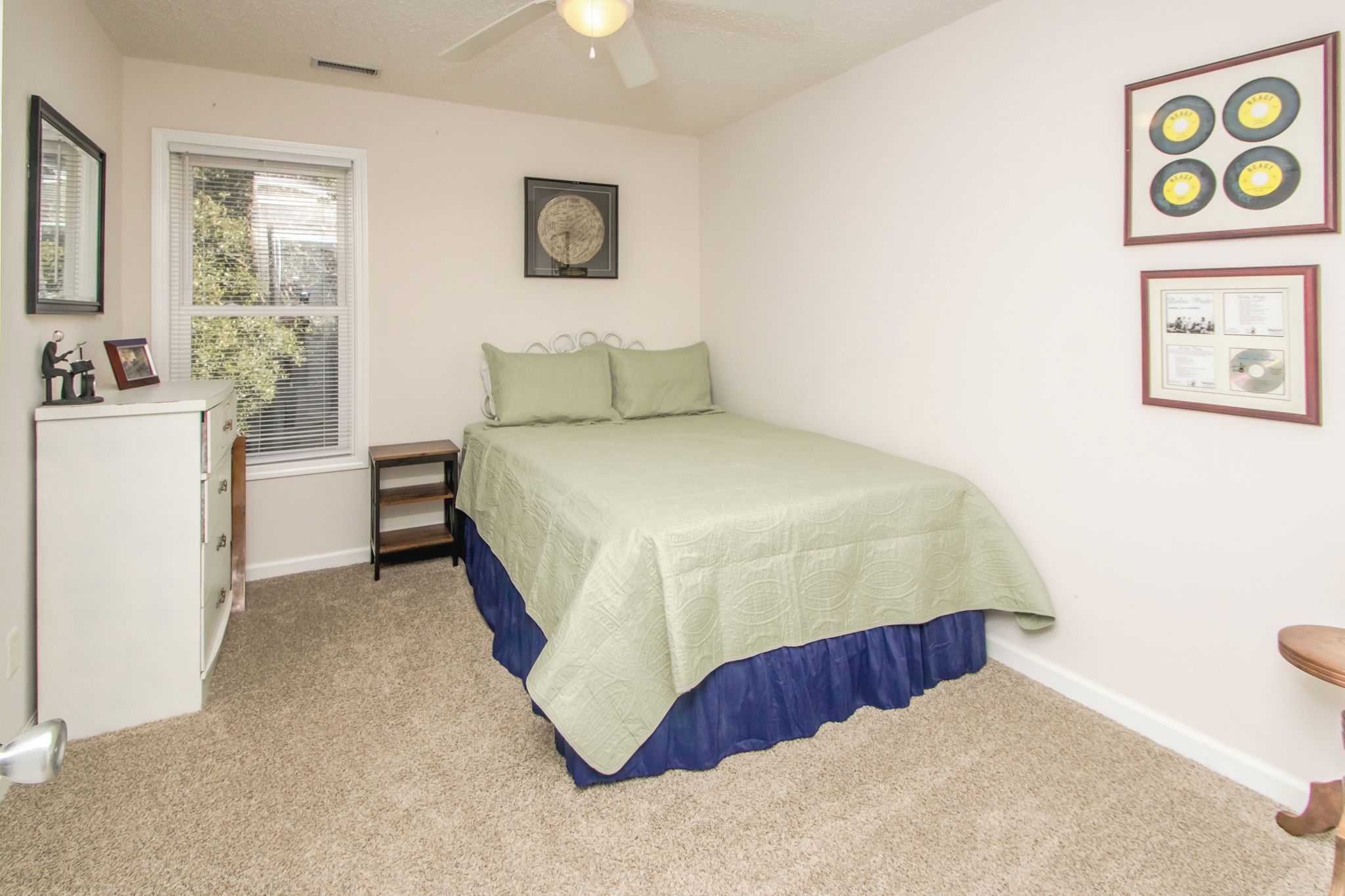 A bedroom with a bed, a desk, a chair, a window, and a ceiling fan.