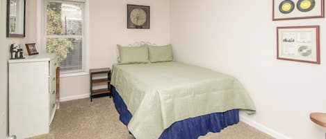 Un dormitorio con cama, escritorio, silla, ventana y ventilador de techo.