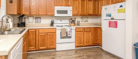 A kitchen with wooden cabinets, a white stove, a microwave, and a refrigerator.