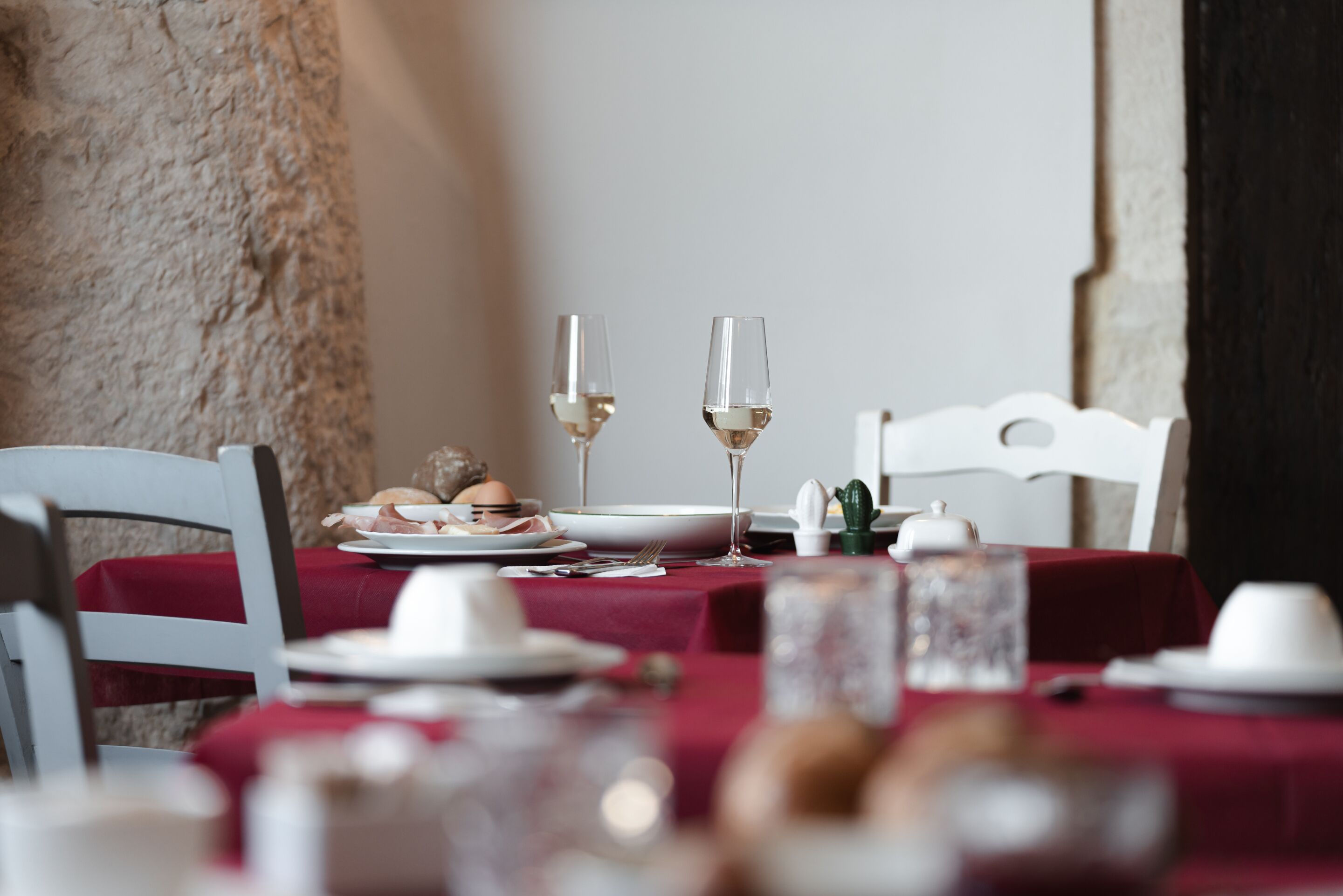 Una mesa de comedor con platos, vasos y cubiertos, con mantel rojo y una silla blanca.