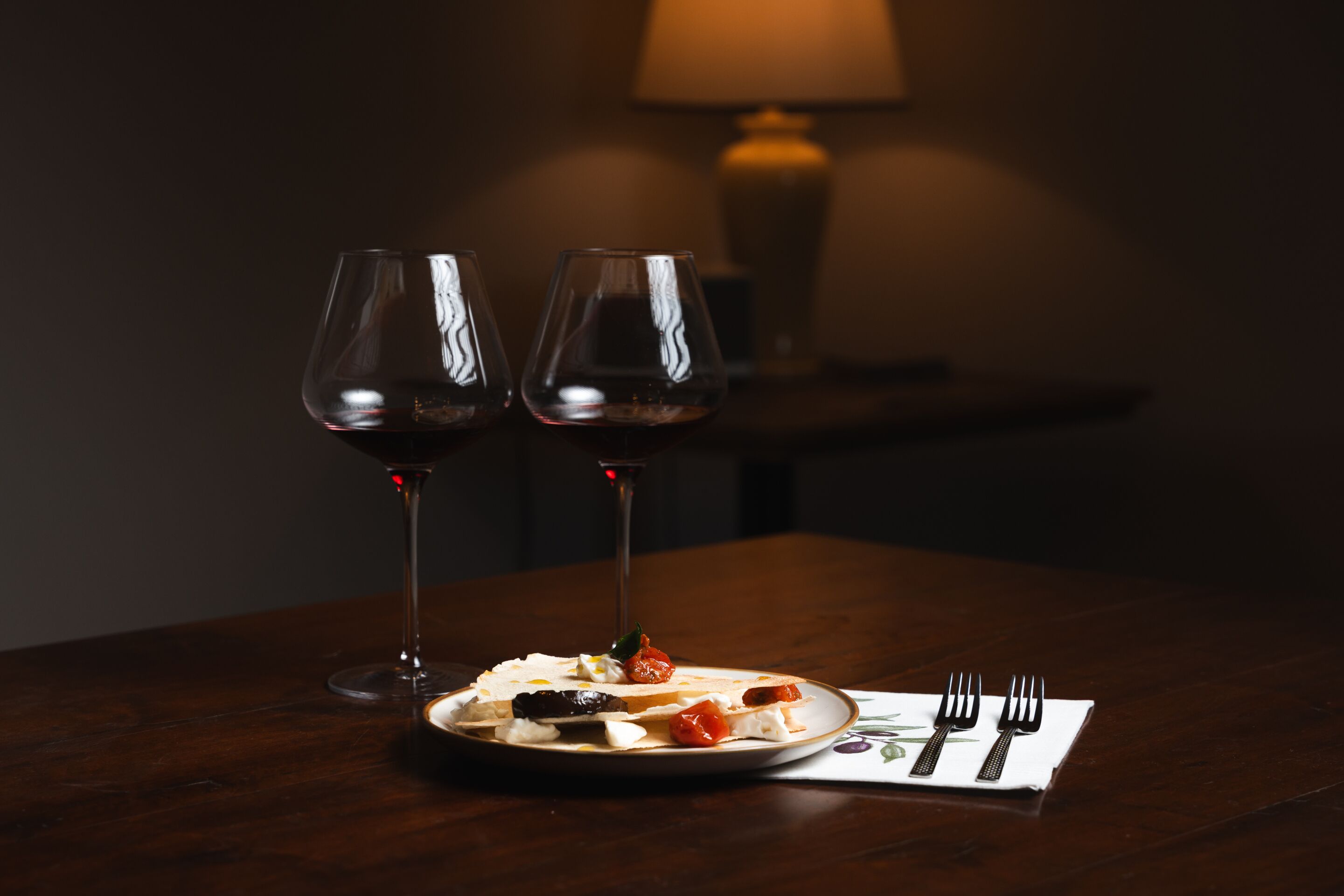 Een eettafel met een bord eten, twee wijnglazen en een servet met bestek.