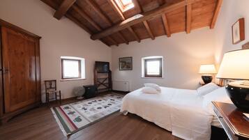 A bedroom with a wooden ceiling, a bed, a nightstand, a lamp, a chair, a radiator, and a window.