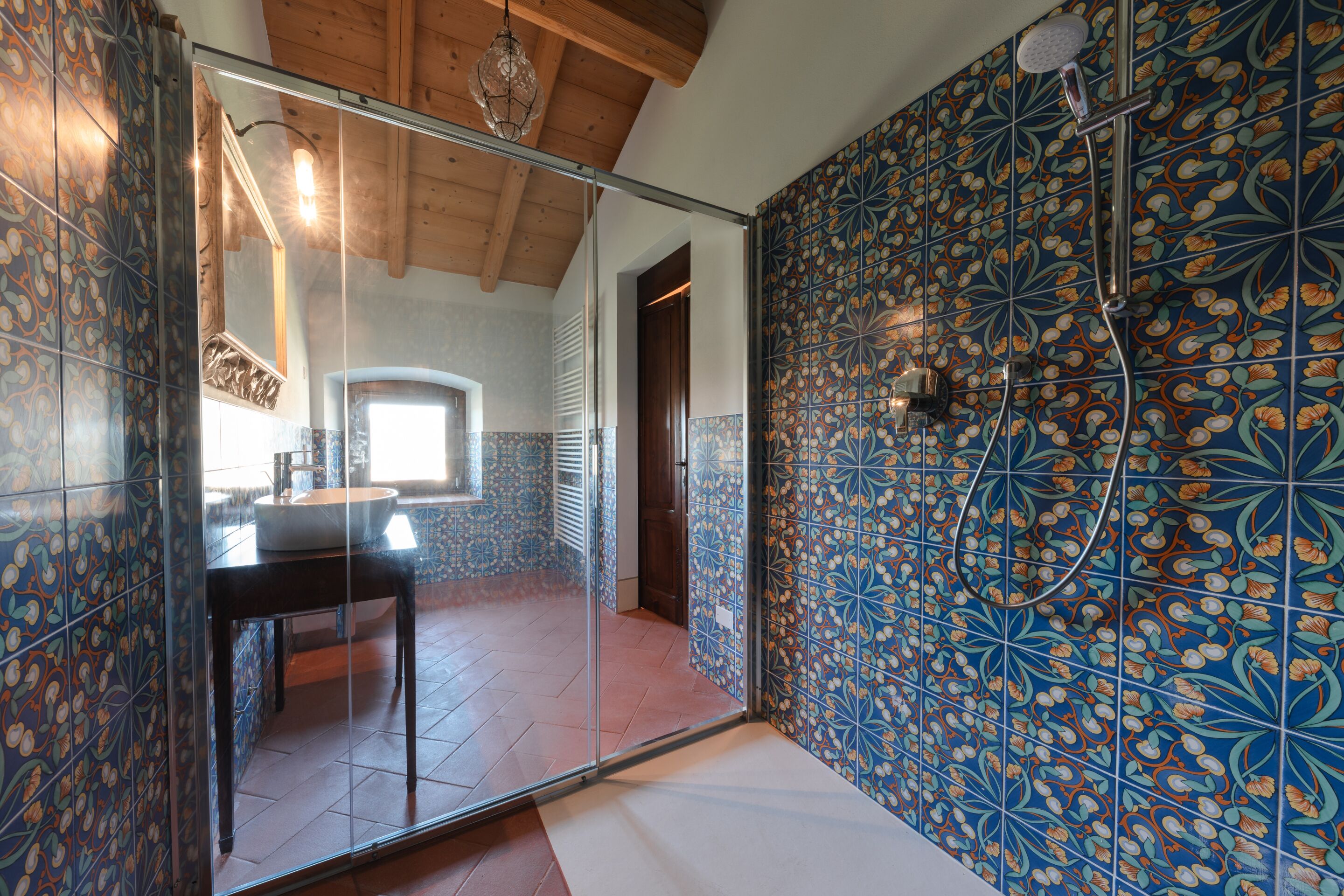 A bathroom with a glass shower door, tiled walls, and a wooden ceiling.