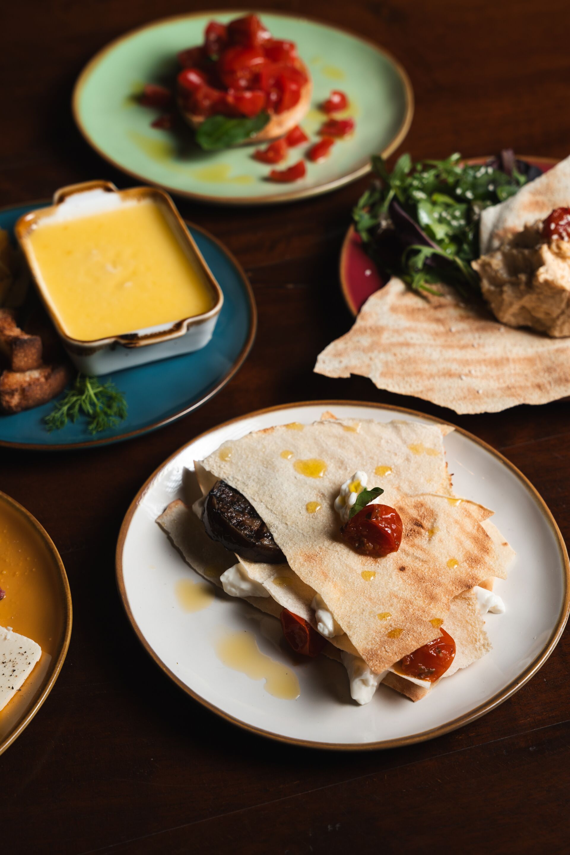 A table with various dishes including a quesadilla, a bowl of soup, and a plate of greens.