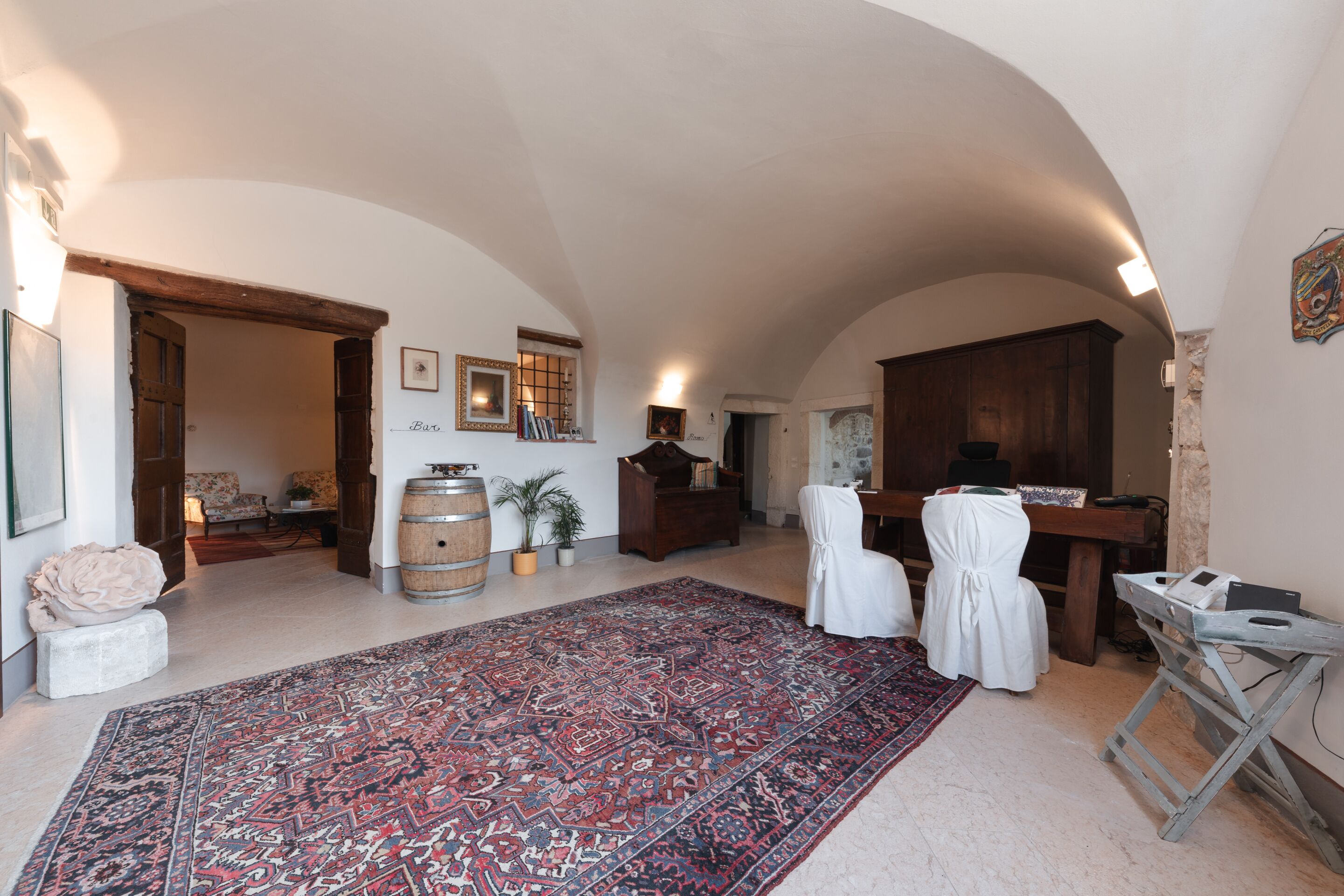 A spacious room with a large patterned rug, wooden furniture, and a rustic ceiling.