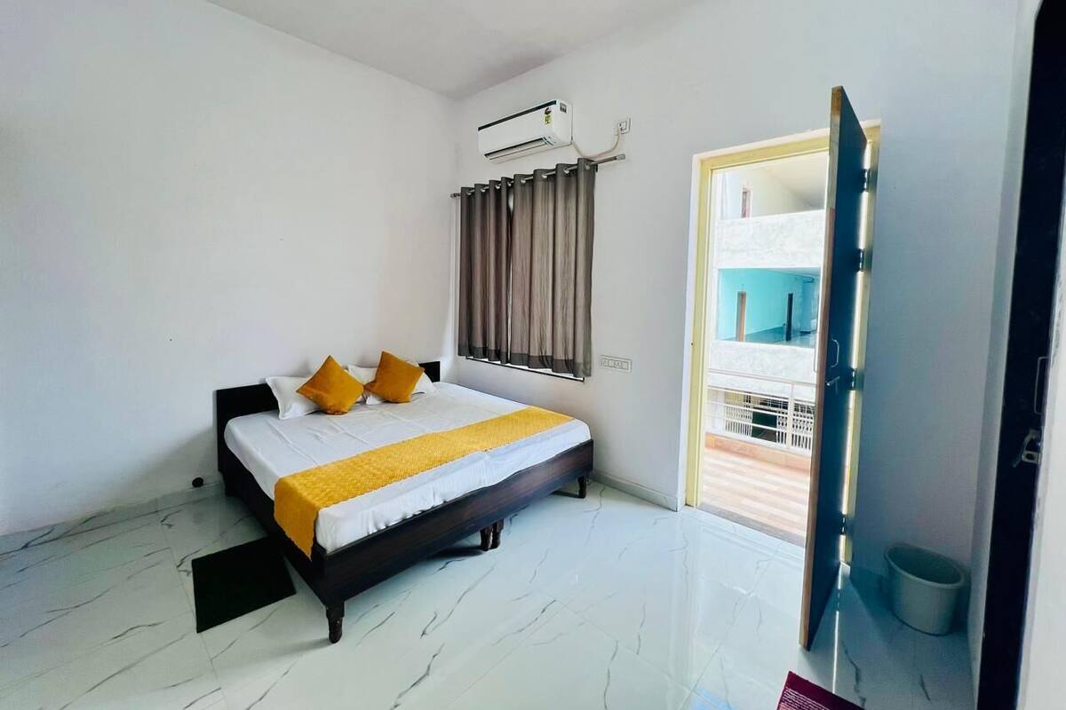 A bedroom with a bed, air conditioning unit, and a view of the outside balcony.