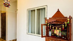 Une pièce avec un meuble en bois orné d’icônes religieuses et une fenêtre avec des rideaux.
