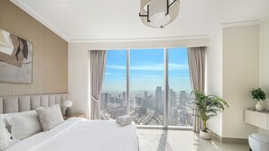 A modern bedroom with a large bed, a city view, and a potted plant.