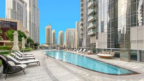 A rooftop pool area with lounge chairs and a small seating area, surrounded by high-rise buildings.