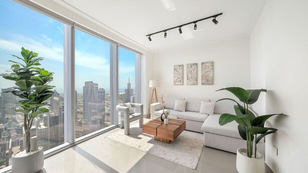 A modern living room with large windows, a sofa, a coffee table, and potted plants.